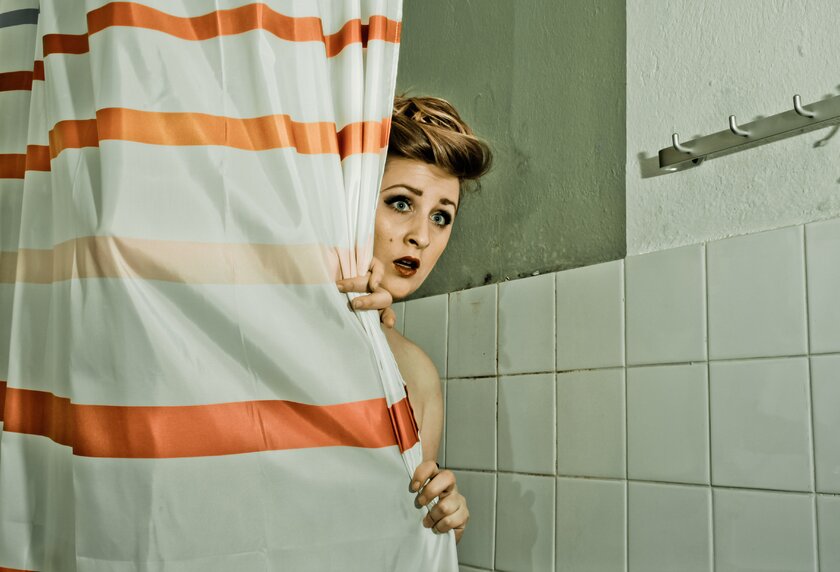 Erschrockene Frau hinter einem Duschvorhang als Hitchcock-Reminiszenz