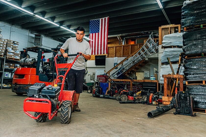 A landscaper pushes a rototiller out of the garage.