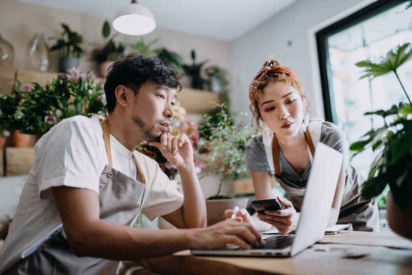 Owners of small business flower store discuss at the counter and calculate figures on the laptop.