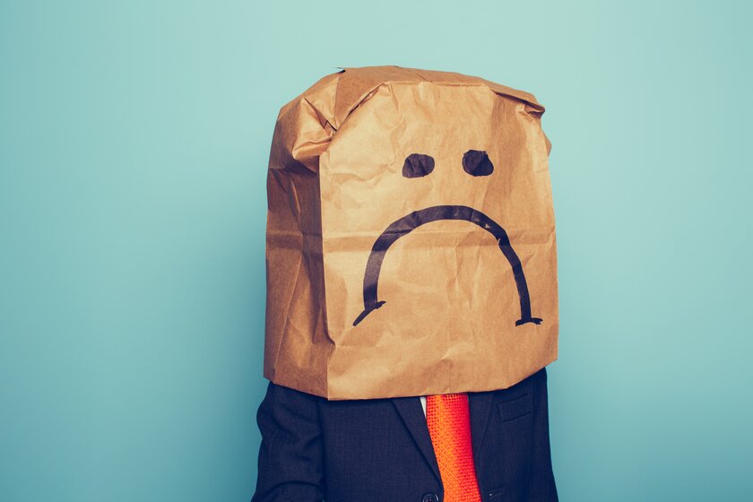  Geschäftsmann mit Papiertüte über dem Kopf und einem traurigen Gesicht darauf als Sinnbild für stockende Geschäfte.