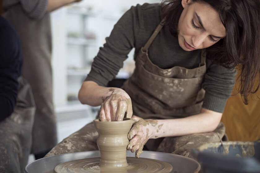 Kunsthandwerkerin ist über eine Töpferscheibe gebeugt und dreht eine neue Vase.