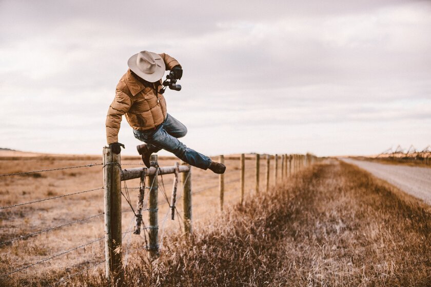 Cowboy swings over barbed wire fence in Montana.