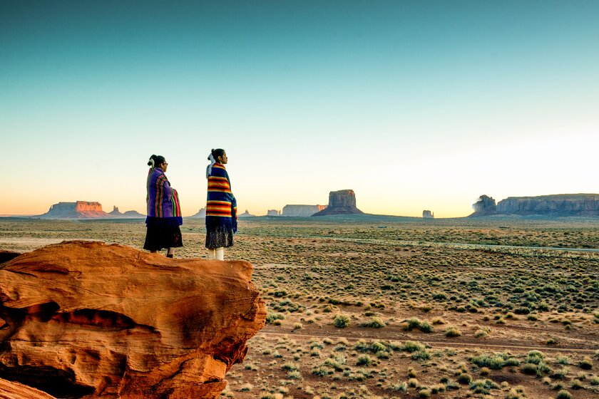Navajo girls wrapped in hand-woven traditional blankets enjoy a great sunrise or sunset in Monument Valley.