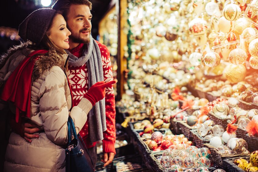 Ein heterosexuelles Paar auf einem Weihnachtsmarkt an einem Verkaufsstand mit Glaskugeln.