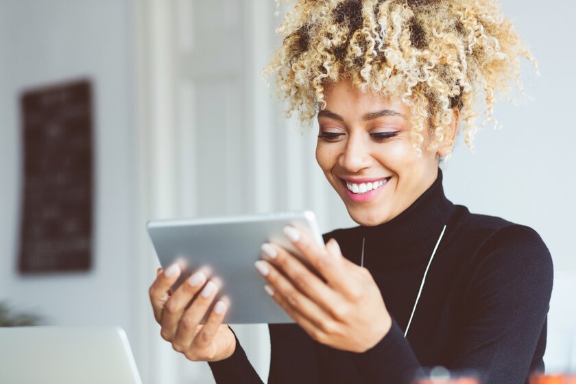 African American woman using a digital tablet in an office, receiving good news and smiling.