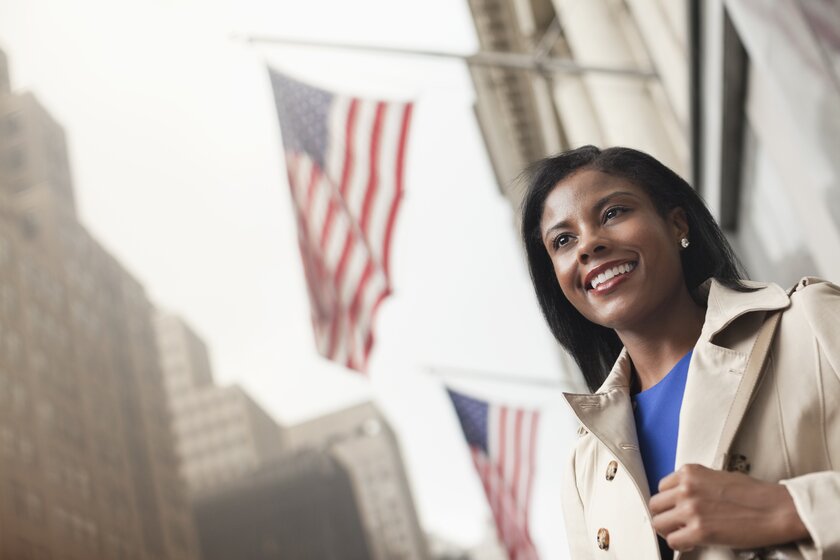 Smiling business woman standing under waving US flag.