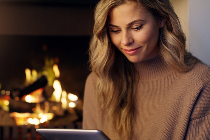 Unternehmerin sitzt am heimischen Kamin und schaut sich ein Webinar auf ihrem Tablet an. 
