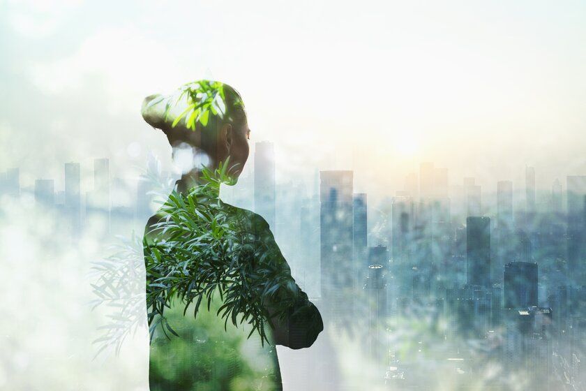 Person standing in contemplation in front of urban city with trees shimmering throughout her body.