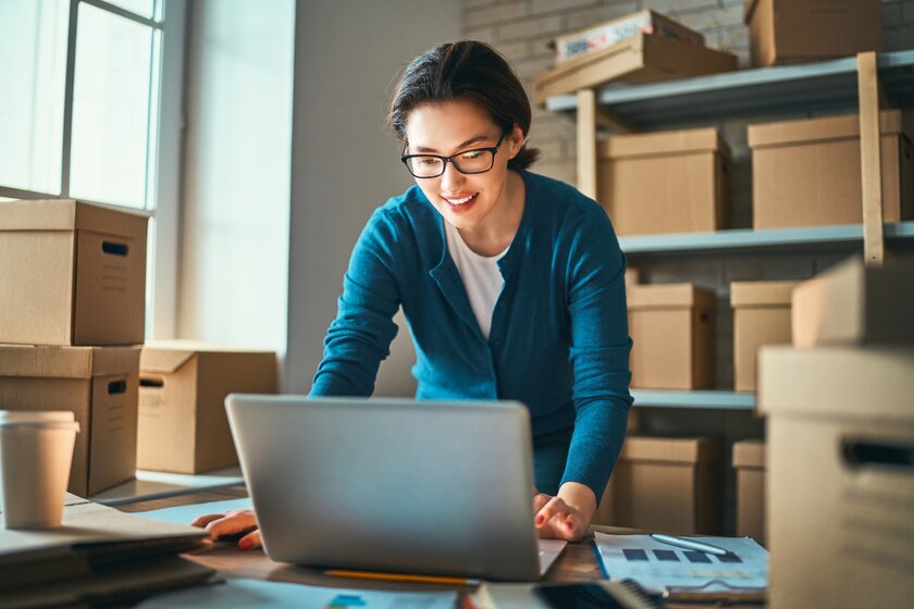 Woman works in her little warehouse surrounded by a bundle of packets. Concept of small web business.