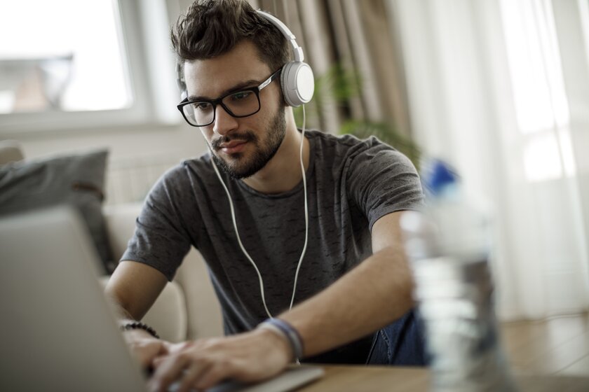 Junger Mann mit Brille und Kopfhörern schaut sich ein Online-Webinar an seinem Laptop an.