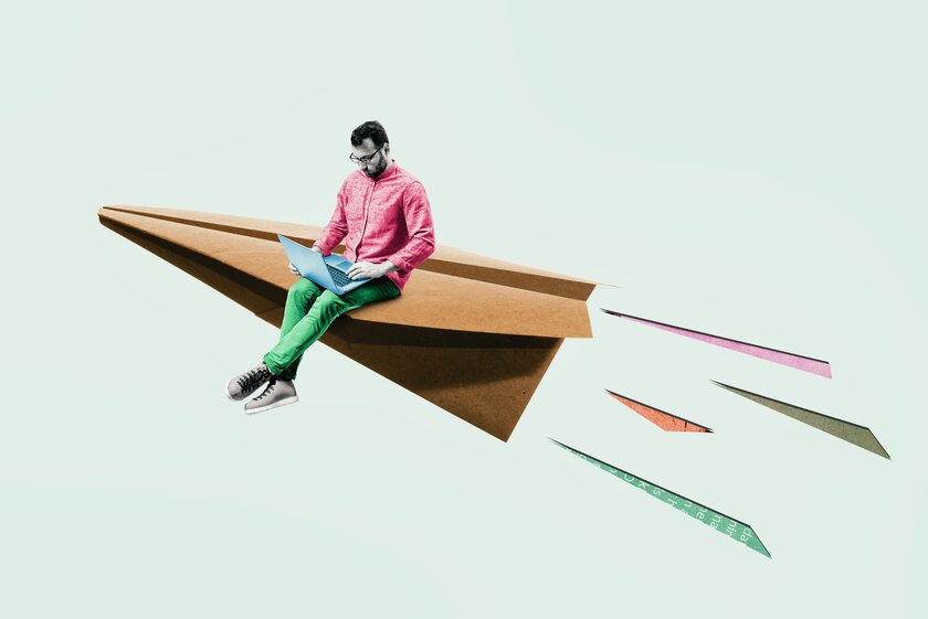 Kunstcollage aus fliegendem Papierflugzeug mit darauf sitzendem jungen Mann an seinem Laptop.