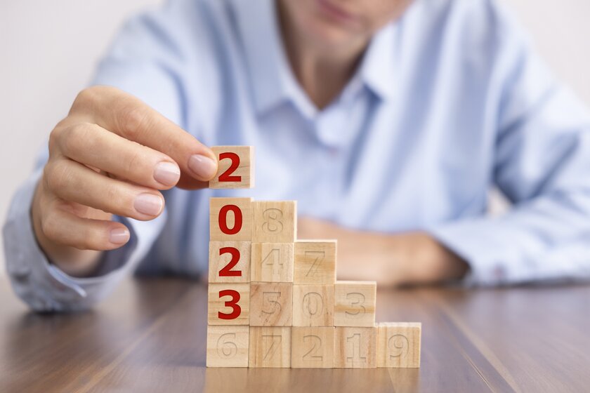 Frau baut aus Dominosteinen einen Block, der die Zahl 2023 hervorhebt als schrittweises Zielkonzept für das neue Jahr.