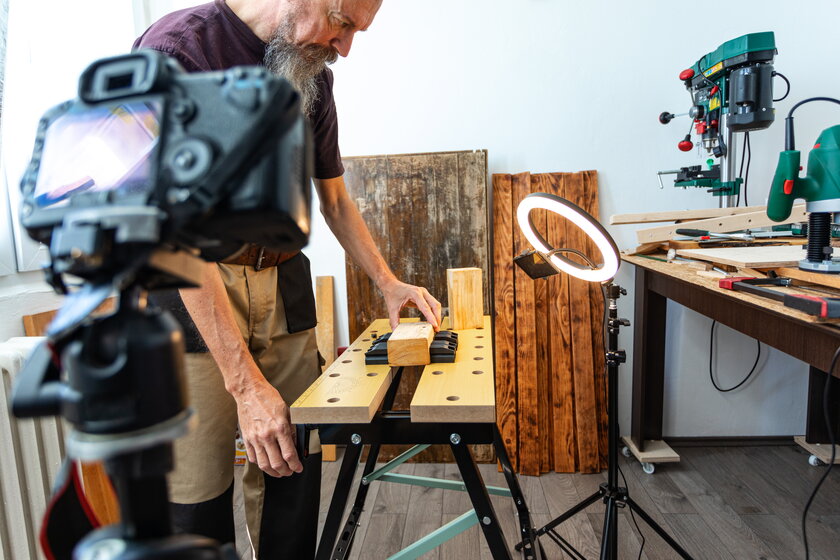 Schreiner bei Holzbearbeitung am Werktisch, links daneben eine Kamera und davor ein Ringlicht zum Videodreh.