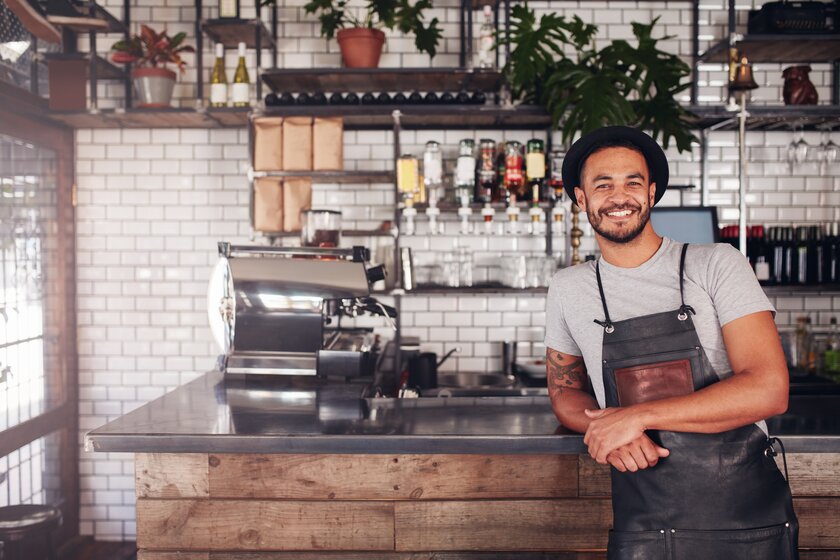 Portrait of a young man standing at the counter in his cafe. 