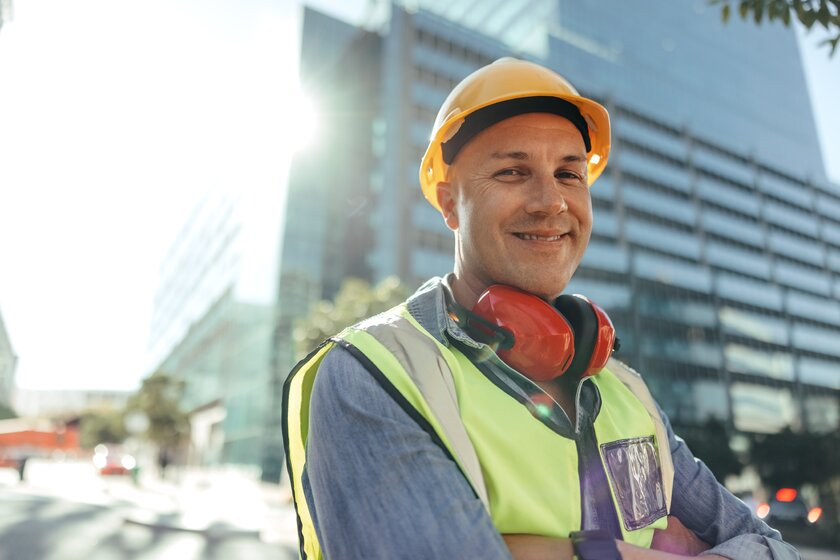 Happy construction worker smiling at camera in front of city scenery.