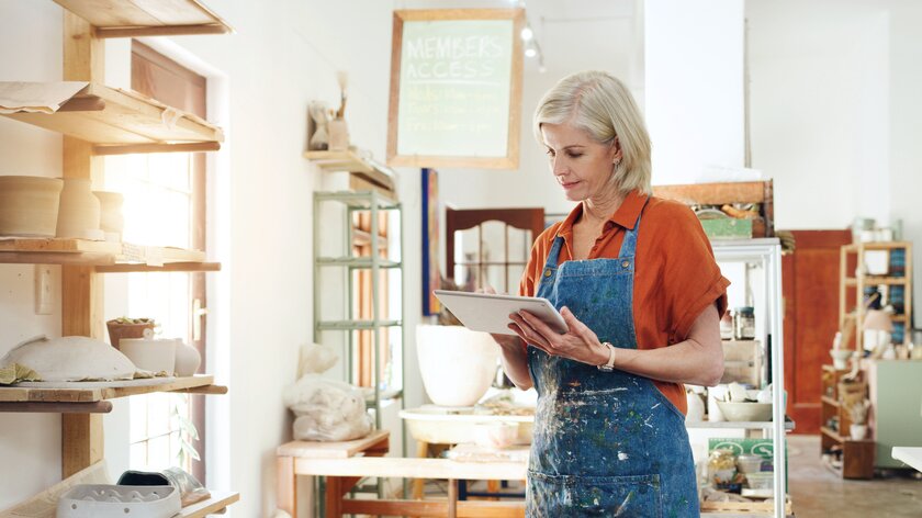 Unternehmerin in ihrer Keramikwerkstatt, prüft Warenbestand im Online-Shop mit Laptop in der Hand.