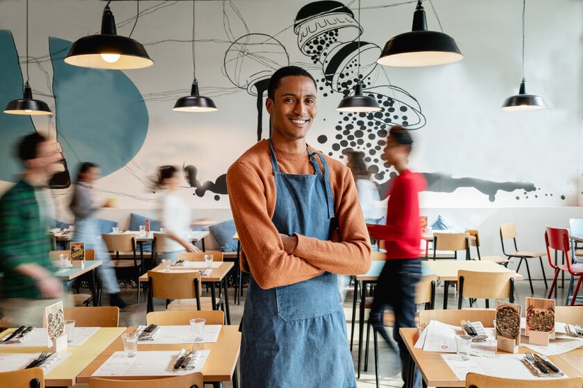 Portrait of male owner in cafe with unrecognizable blurred employes moving.