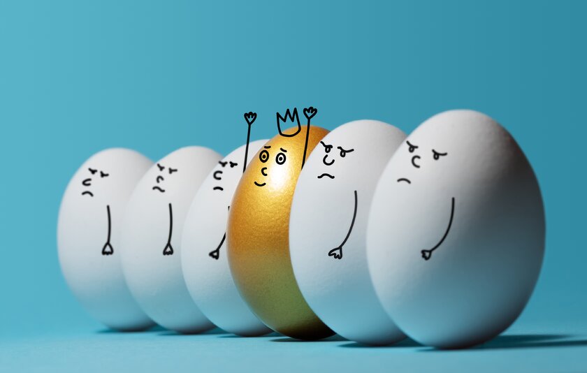 Sechs weiße Eier mit bemaltem Trauergesicht rahmen ein lachendes goldenes Ei.