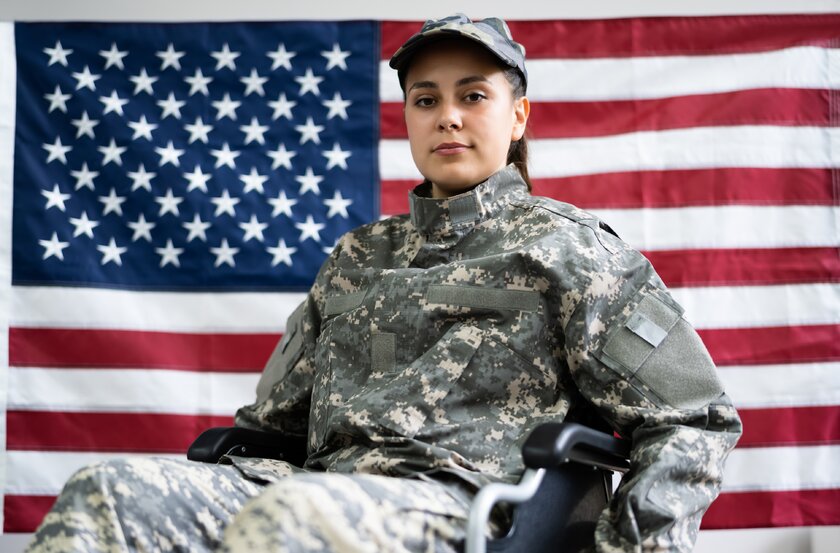 A female veteran sitting in a wheelchair in front of U.S. flag.