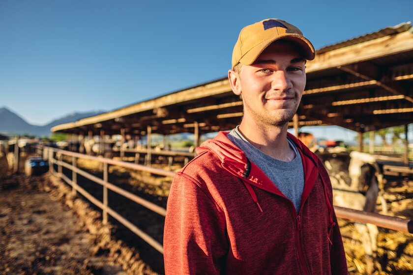 A young farmer at the cowshed is smiling in the morning sun.