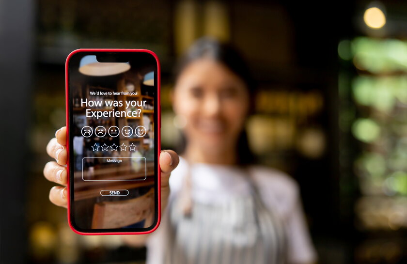 Gastronomin im Hintergrund zeigt Smartphone App mit Aufforderung zu Online Bewertung.