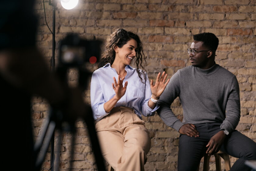 A woman and a man shooting a short video for TikTok smile and gesture with their hands as they speak.