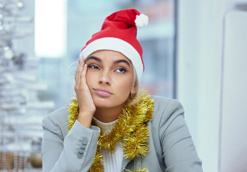 Aufnahme einer traurigen jungen Frau, die mit Weihnachtshut auf dem Kopf das Gesicht verzieht.