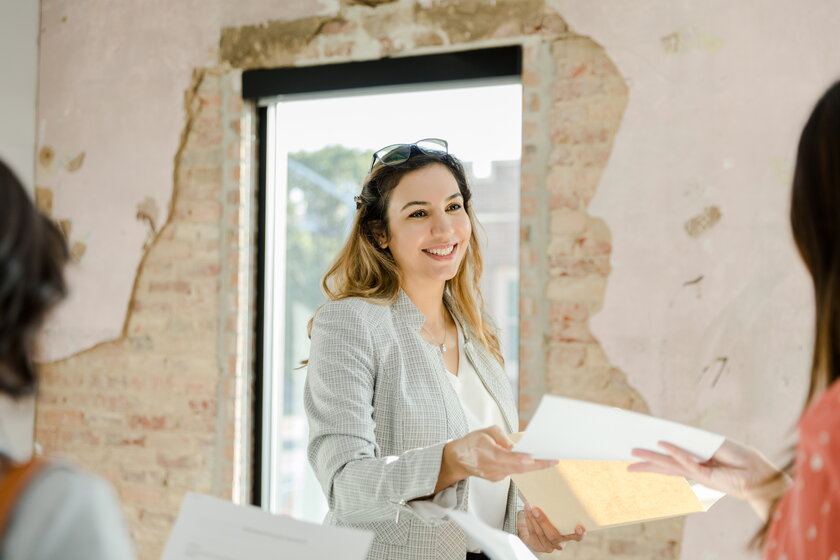 Smiling real estate agent hands brochure at property viewing.