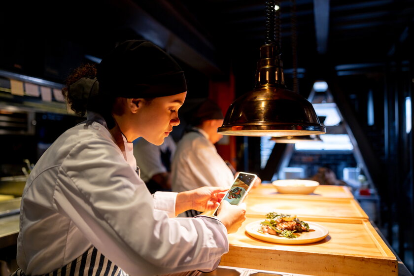 Cook taking a picture of a plate in a restaurant with her cell phone.