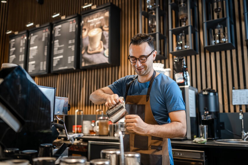 Male barista makes coffee for customers at the bar.