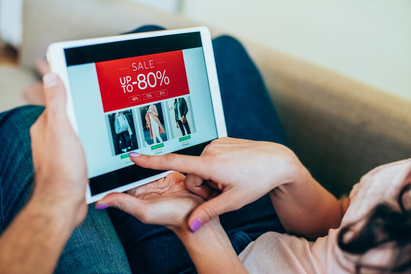 Tablet in der Hand eines Paares auf der Couch sitzend beim Einkaufen von Kleidung online.