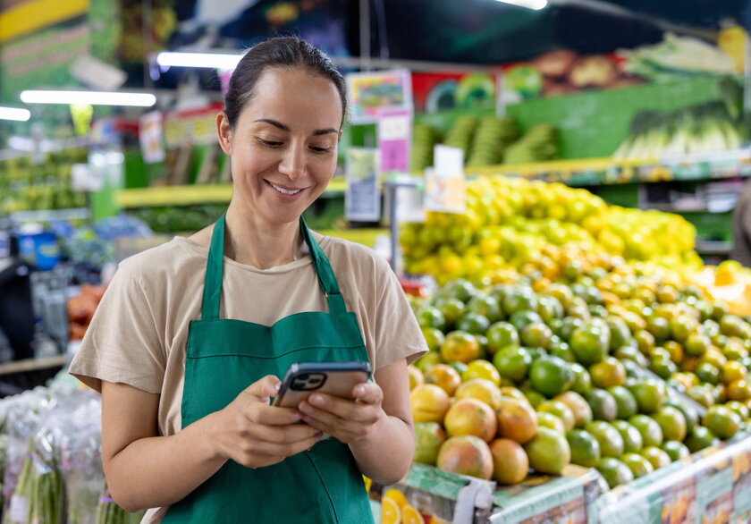 Einzelhandelsunternehmerin, die ihr Telefon benutzt, waehrend sie im Supermarkt arbeitet.
