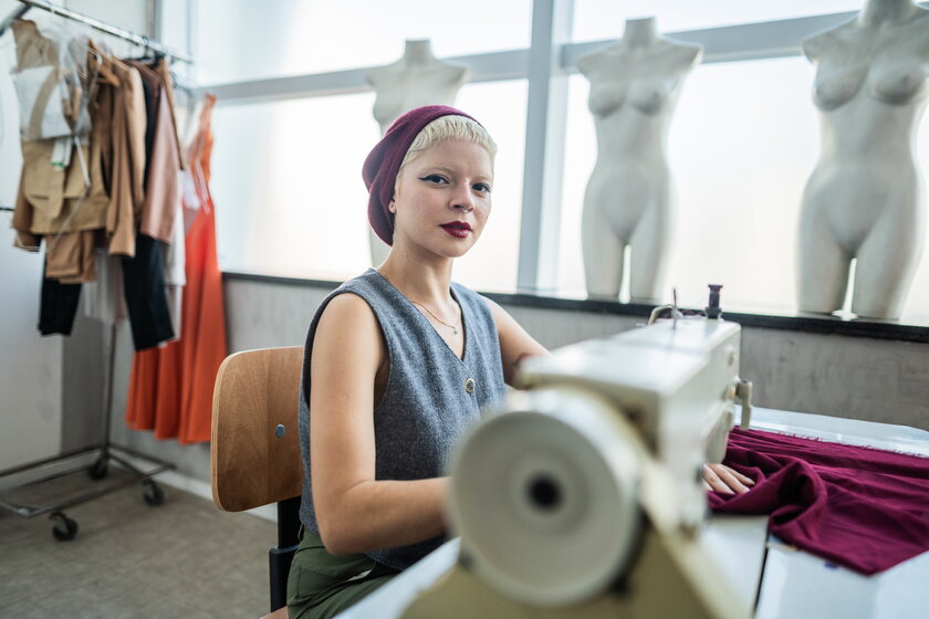 Junge Modedesignerin sitzt an einer Naehmaschine in ihrem Atelier.