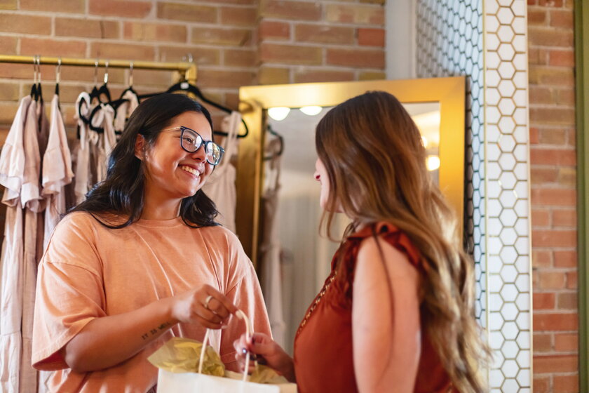 Boutique owner with long hair and glasses talking to a customer.