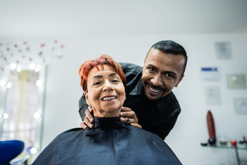 Friseur, der eine laechelnde Kundin im Schönheitssalon betreut.