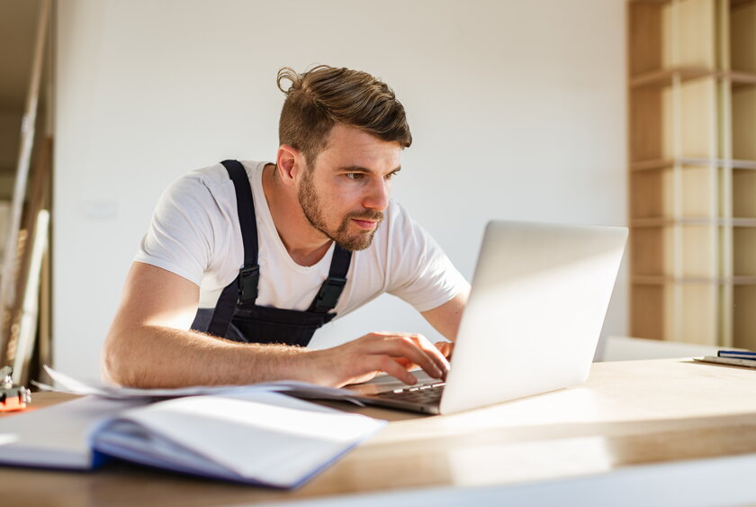 Junger Tischler mit Computer auf der Baustelle.