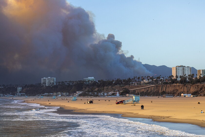 An intense wildfire blazing through a hillside in Pacific Palisades, Los Angeles as viewed from the beach.