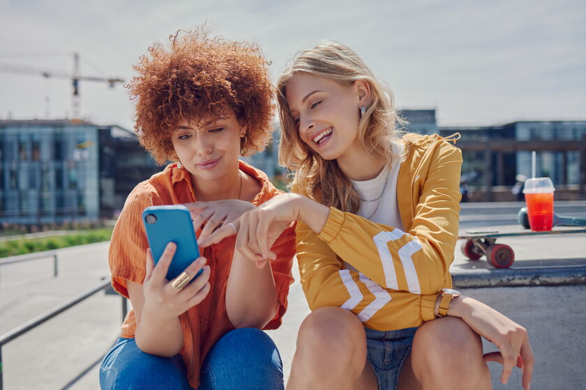 Skaterinnen im Park lachen über ein Meme auf dem Smartphone.