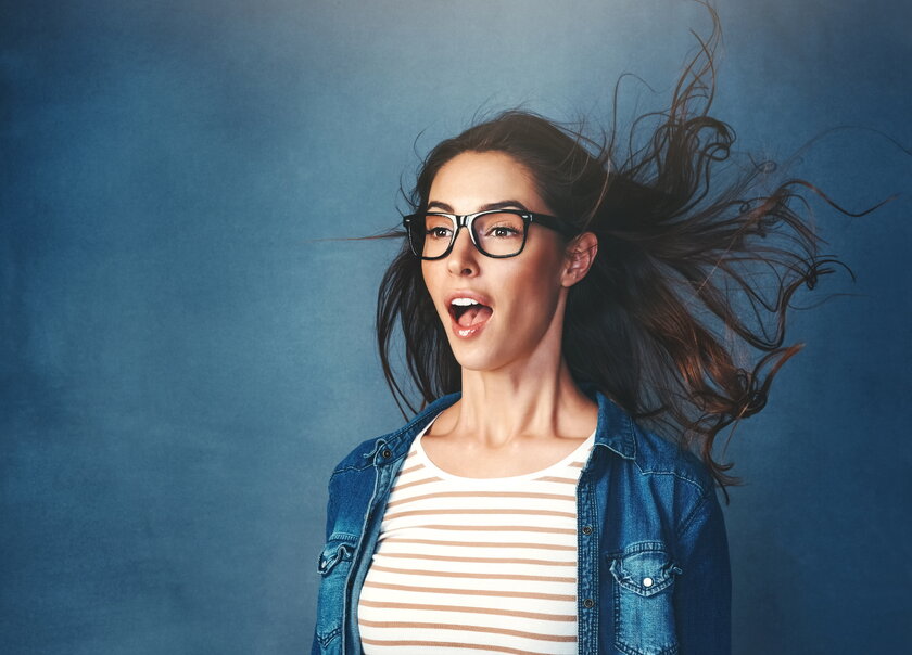 Studioaufnahme einer jungen Frau mit Brille, offenem Mund und wehendem Haar.